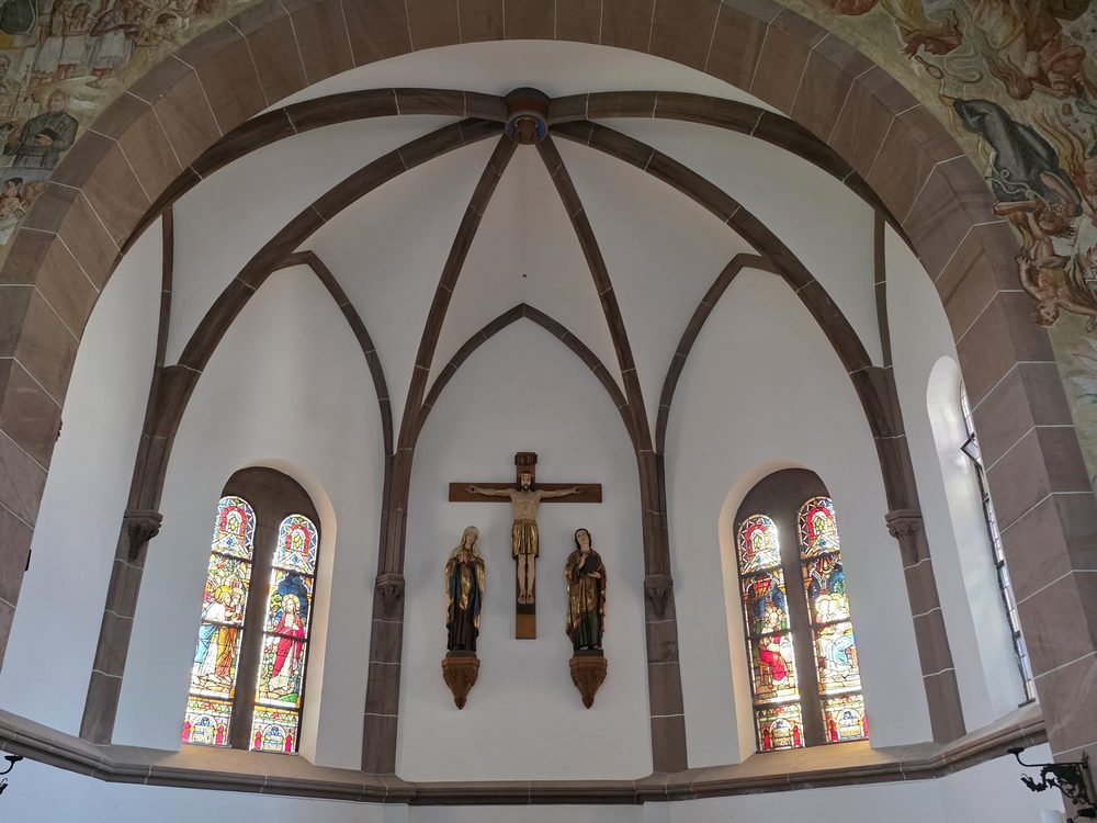 Chorraum – Kruzifix, Buntglasfenster und Sandsteinbogen vor ruhigen, hellen Flächen